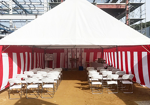 赤白の垂れ幕がかかったテントと白い布が掛けられたパイプ椅子